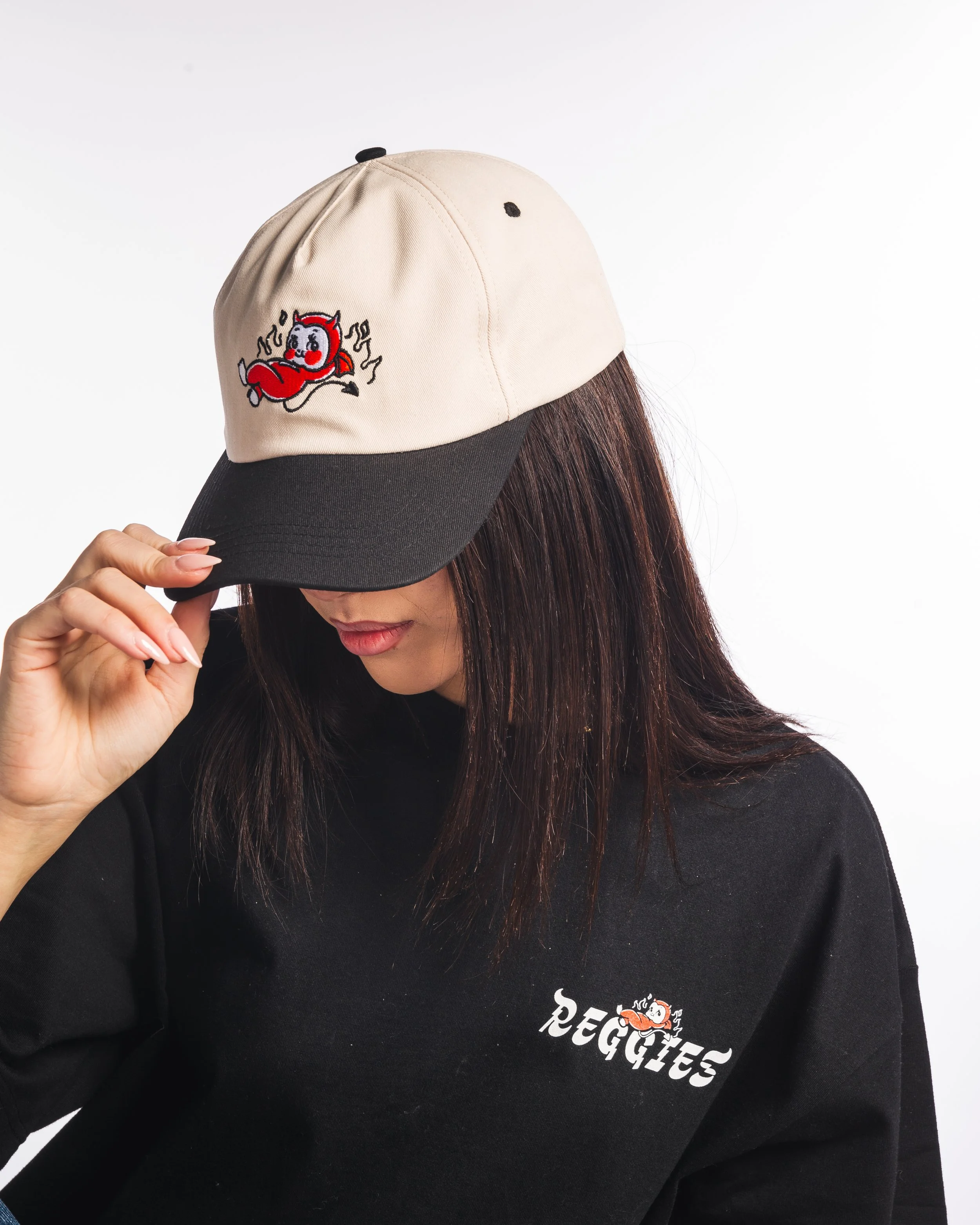 Woman wearing a black sweatshirt and beige and black cap with a cartoon image of a red devil.