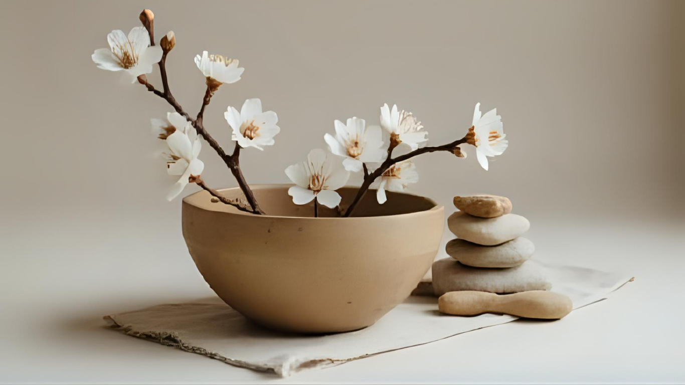 Weiße Blüten in einer braunen Schüssel mit Steinen daneben, auf einer cremefarbenen Oberfläche.