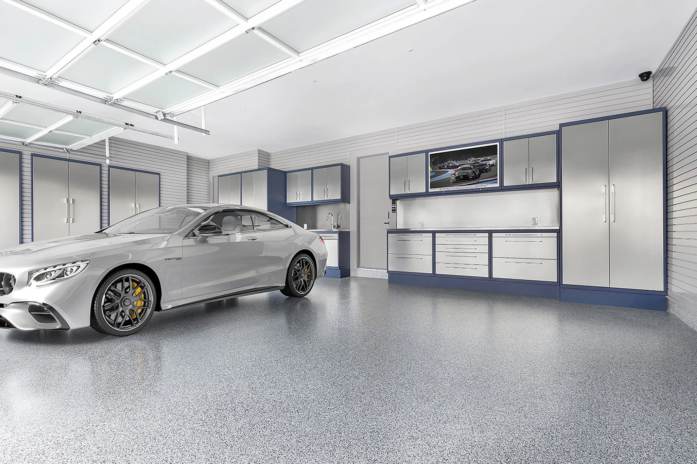 A modern garage with a silver luxury car, cabinetry, and a TV mounted on the wall.