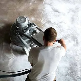 Person operating a floor buffer machine on a shiny, wet concrete floor.