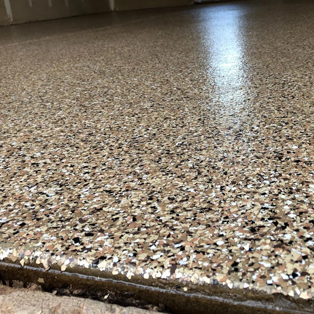 Close-up of a speckled terrazzo floor with brown, black, white, and beige chips, polished to a shine.