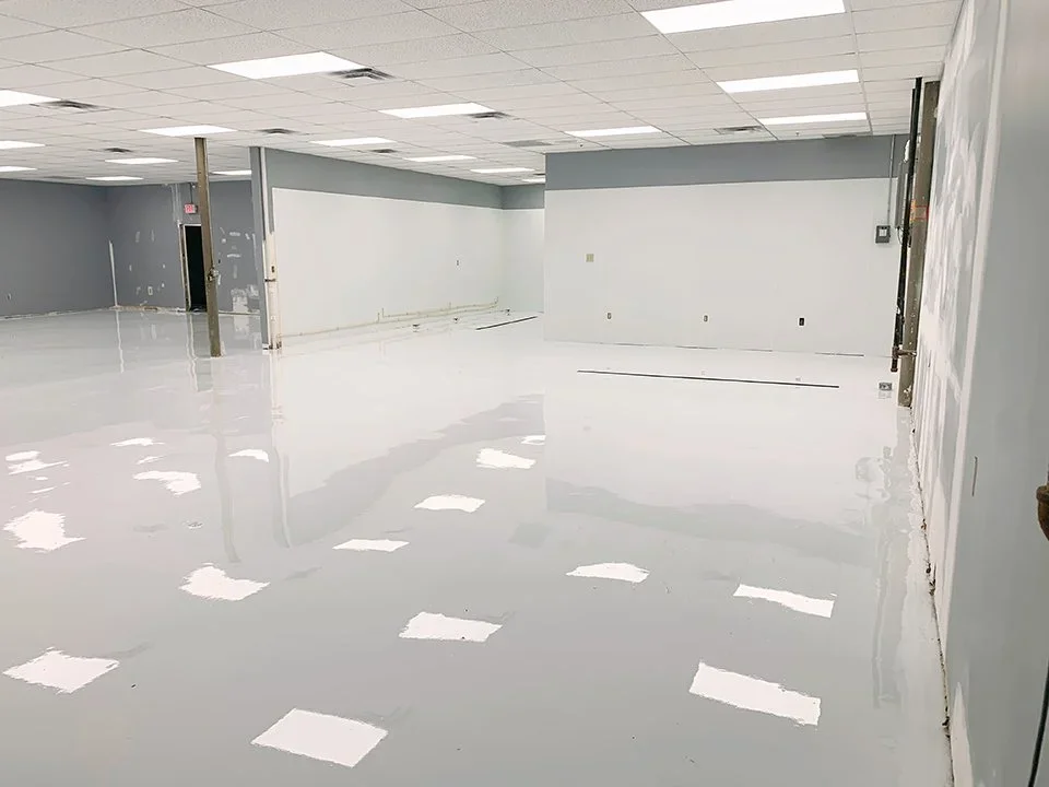 Empty commercial space under renovation with a glossy white floor and partially painted walls.