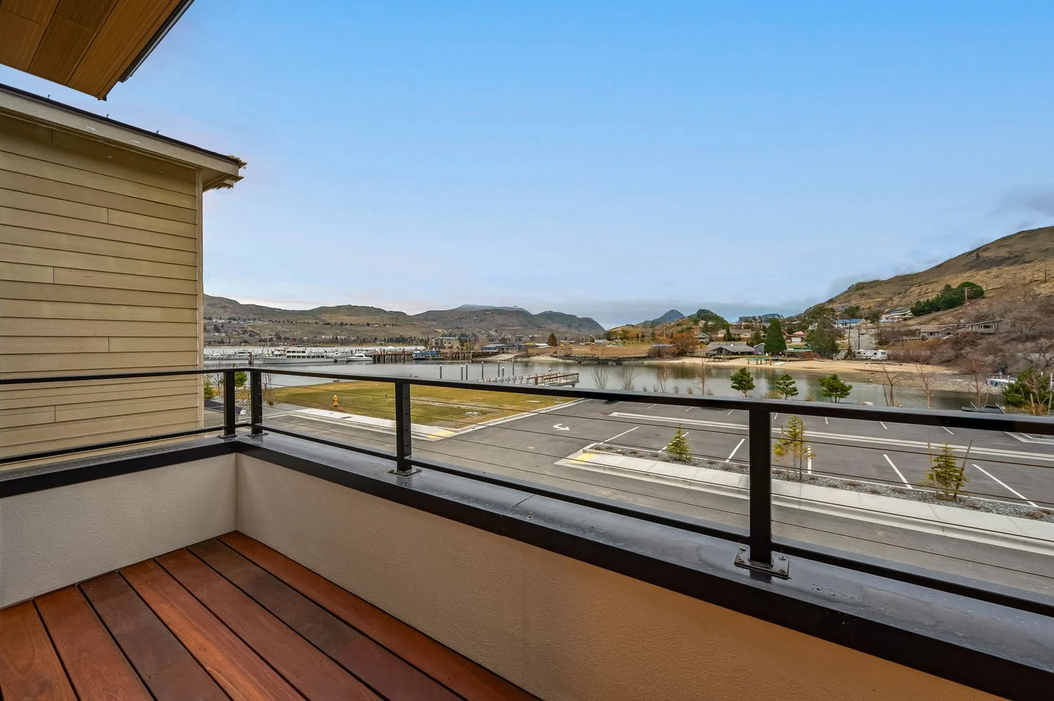 View from a balcony overlooking a parking lot, a body of water, and distant hills with houses and trees under a cloudy sky.