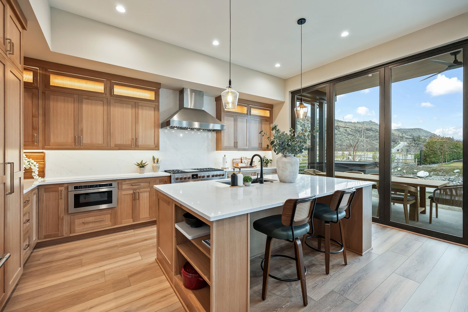 Modern kitchen with wooden cabinets, white countertops, a center island with a sink, and large sliding glass doors opening to a scenic outdoor view.