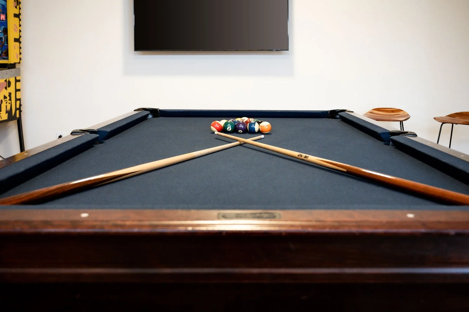 Billiards table with pool balls racked at the far end and two cue sticks crossed on the table.