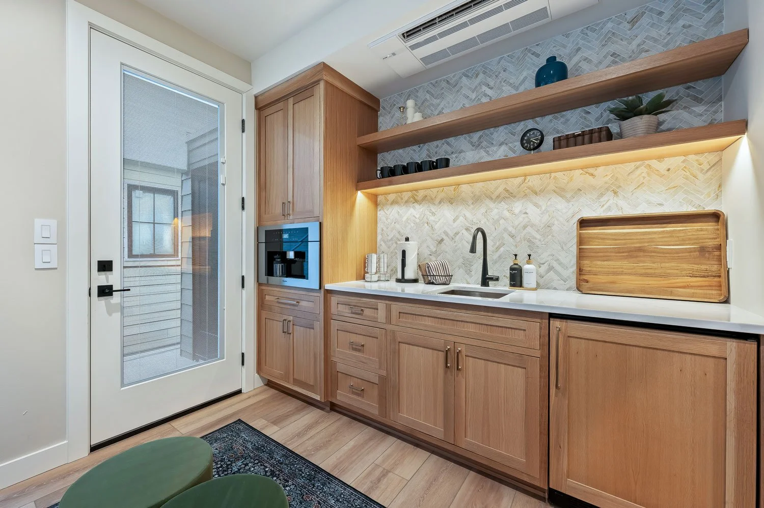 Kitchen with wooden cabinets, a white countertop, open shelves with decor, a black faucet, a sink, a coffee machine, and a door with glass and a screen.