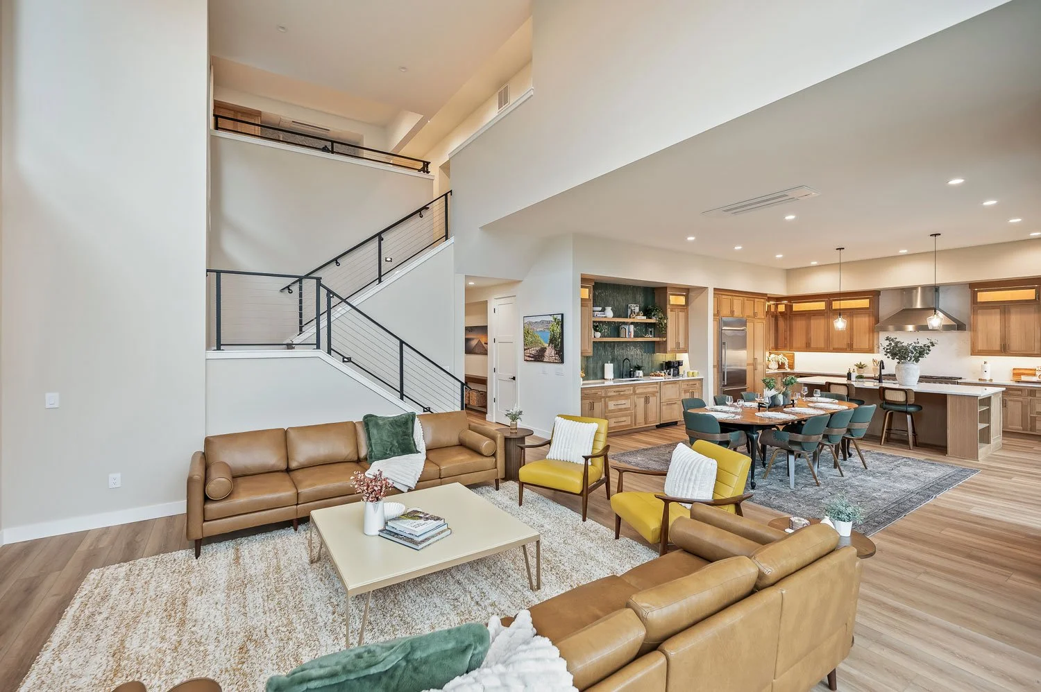 Open-concept living room and kitchen with leather sofas, yellow armchairs, dining table, wooden cabinets, and modern lighting.