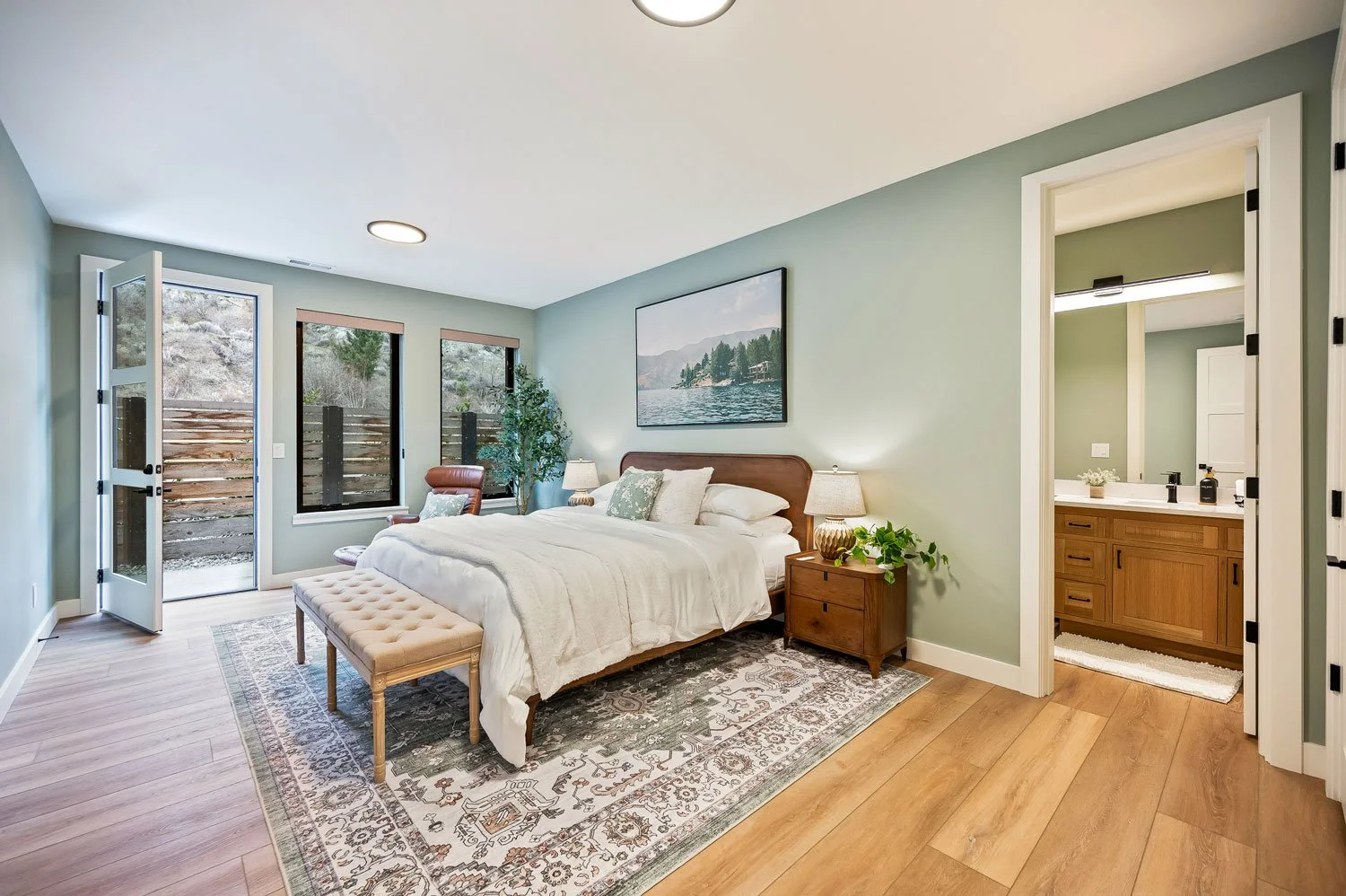 A bedroom with a large bed, nightstands, lamps, and a window view of outdoor patio and landscape.