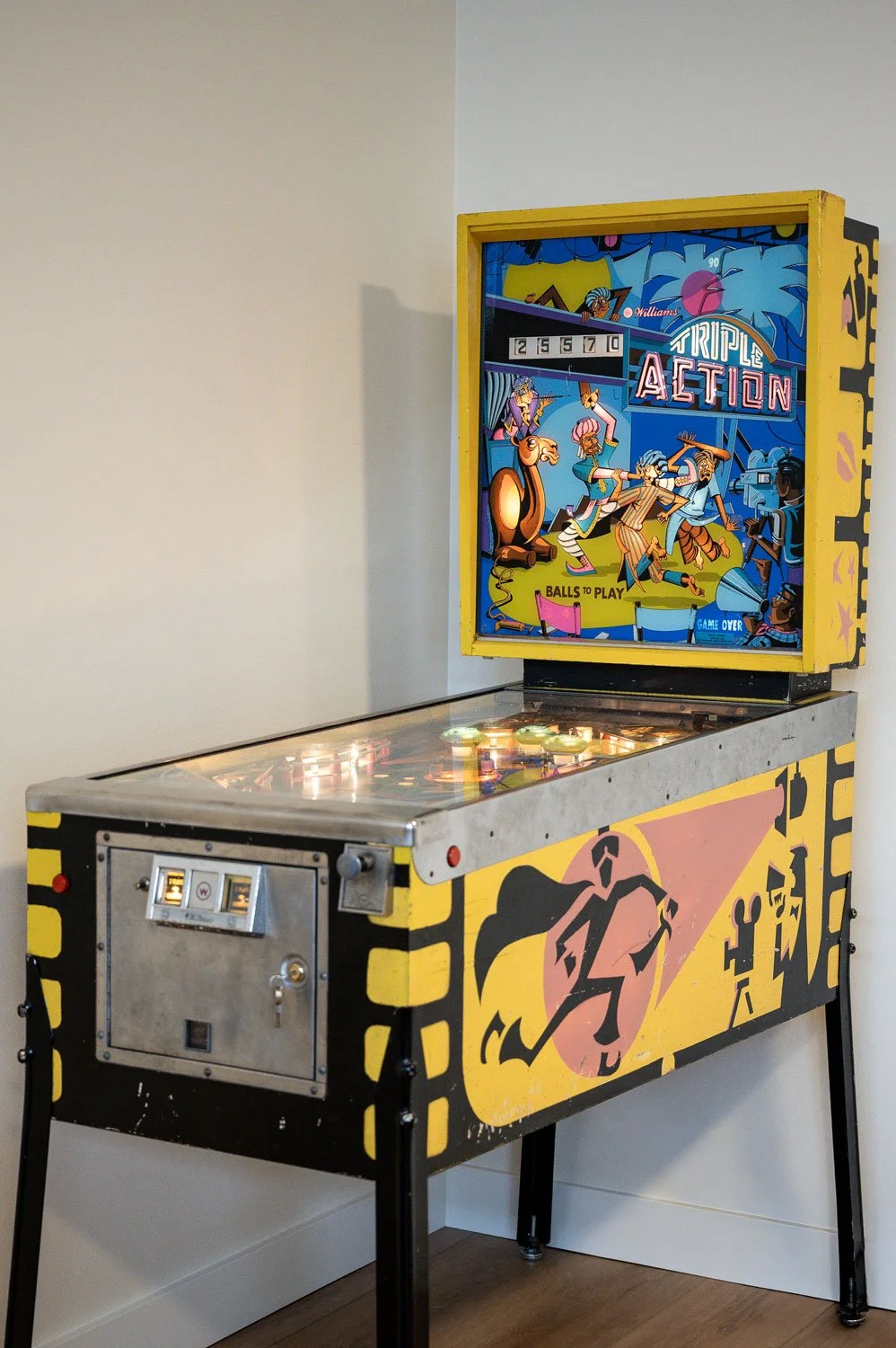 A vintage pinball machine with a yellow and black design, featuring a colorful backglass display with cartoon characters and the words "Triple Action".