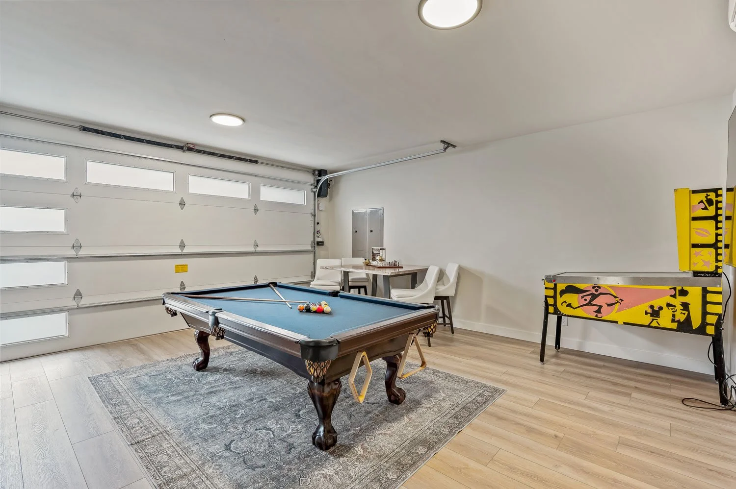 Garage converted into game room with pool table, pinball machine, three chairs, lamp, and small table.