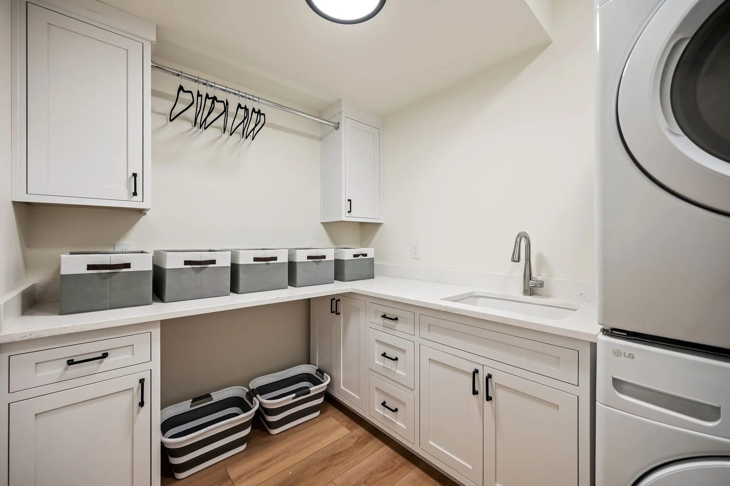Laundry room with white cabinets, countertop, laundry baskets, a hanging rod with hangers, a sink, and an LG washer and dryer.