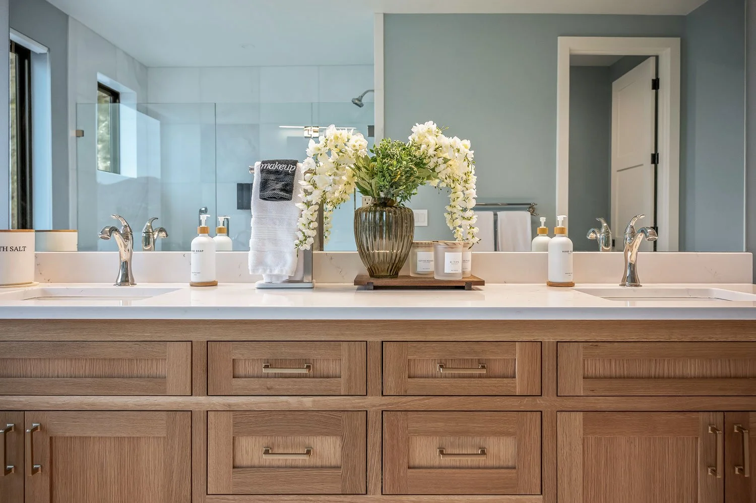 Bathroom vanity with double sinks, large mirror, and a vase with white flowers on the countertop.
