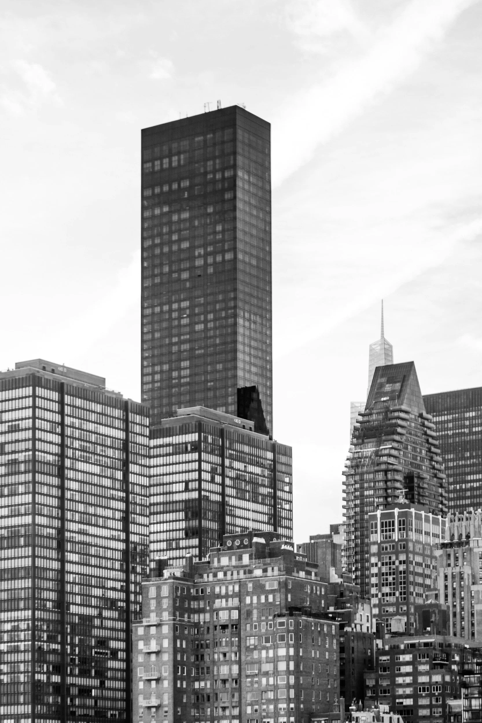 Black and white photo of a city skyline featuring tall skyscrapers, including a prominent high-rise building with a grid-patterned facade, surrounded by other modern buildings with various architectural styles.