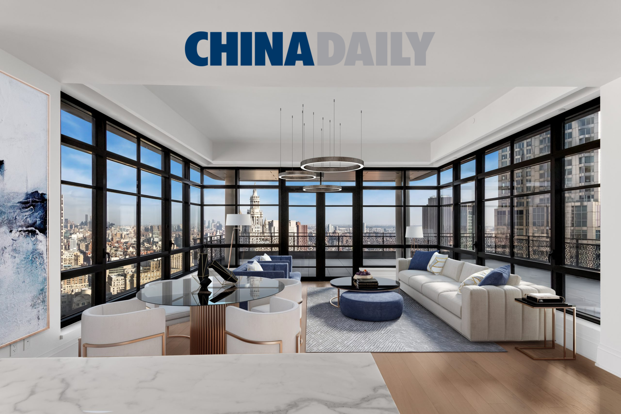 Modern living room with large floor-to-ceiling windows showcasing a city skyline, including a historic building. The room has a white sofa, blue armchair, round blue ottoman, and a dining table with white chairs, all on a light-colored rug with wooden flooring.