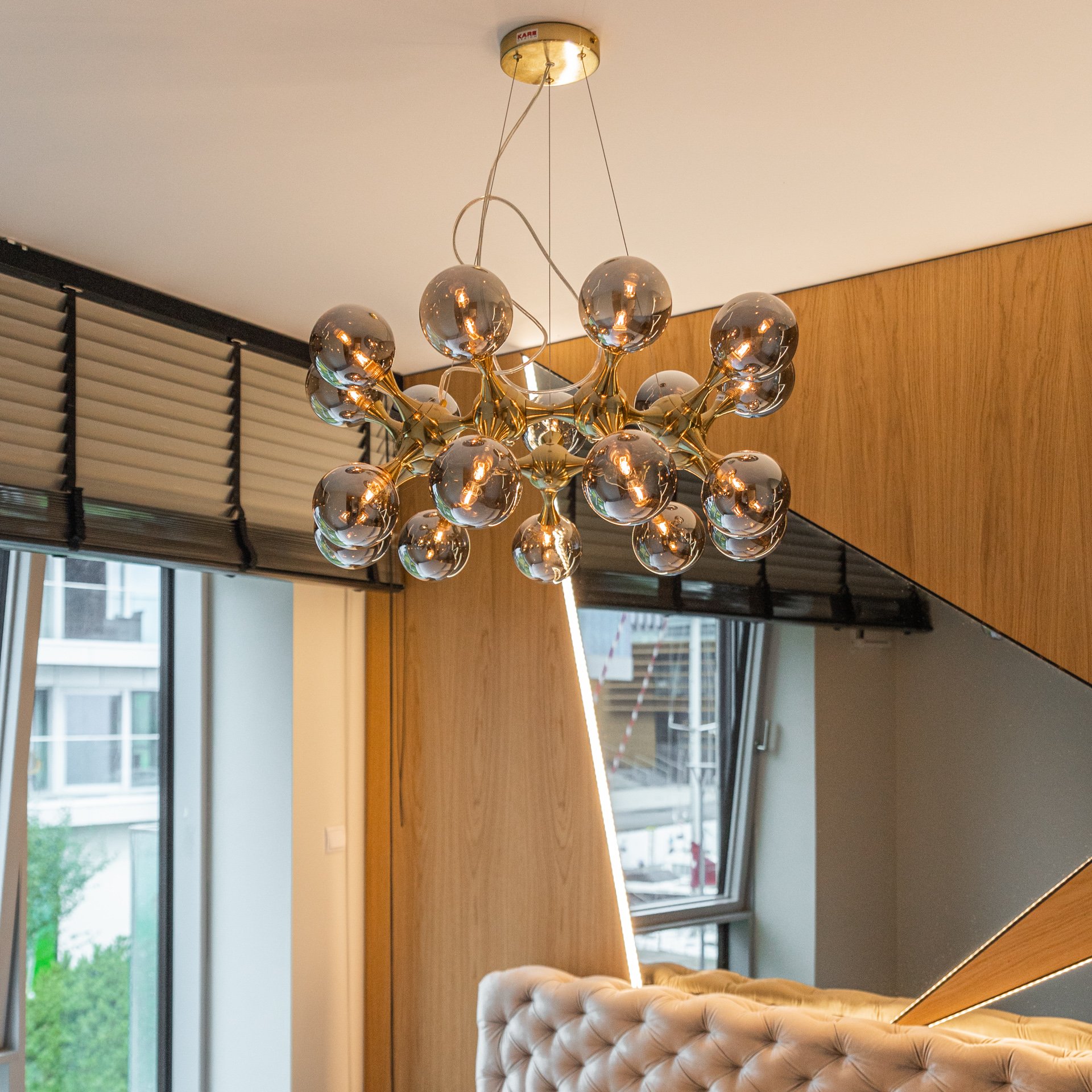 Modern chandelier with multiple spherical glass bulbs hanging from a gold fixture in a contemporary room with wood paneling and large windows.