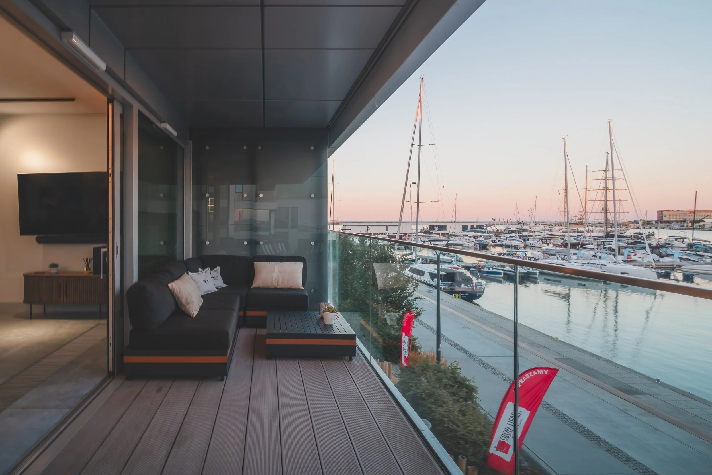 Balcony with black sofa and pillows overlooking marina with sailboats at sunset