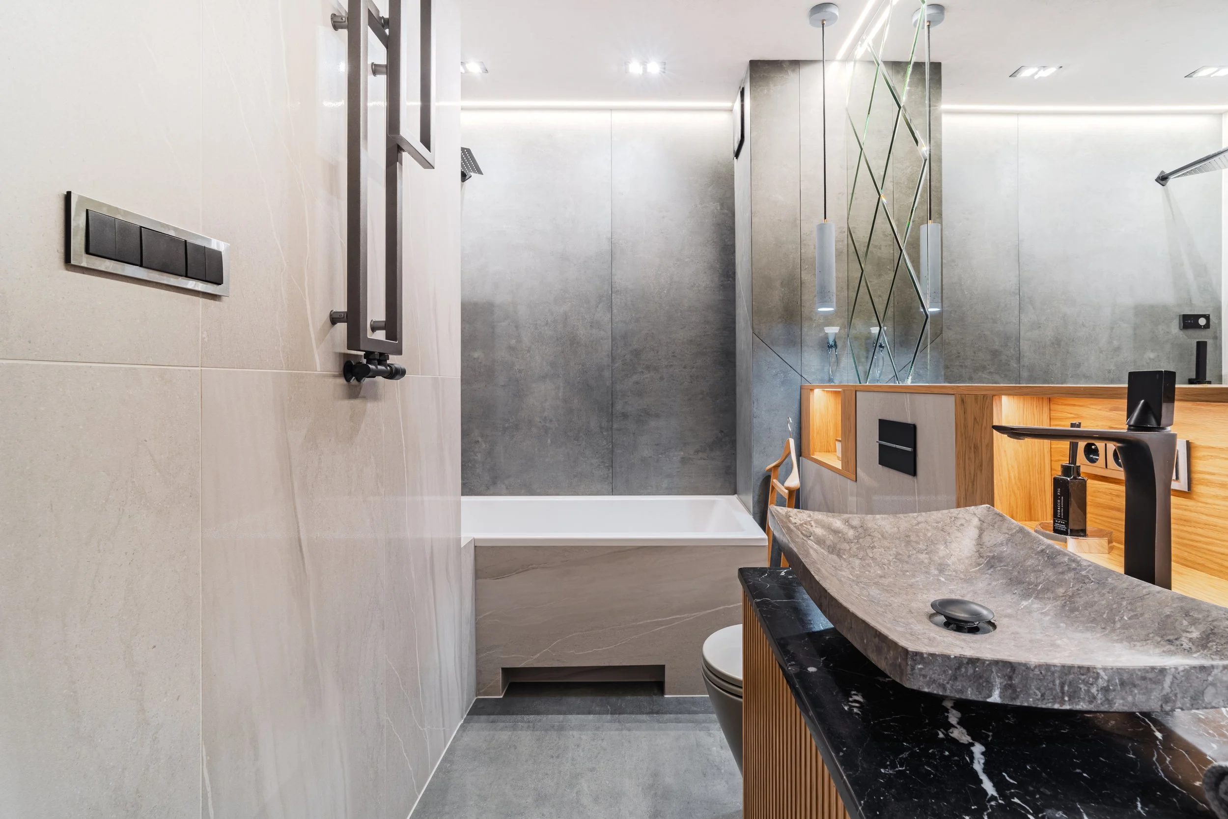 Modern bathroom with concrete walls, a wooden vanity, a unique stone sink, black fixtures, and a walk-in shower with grey tiles.