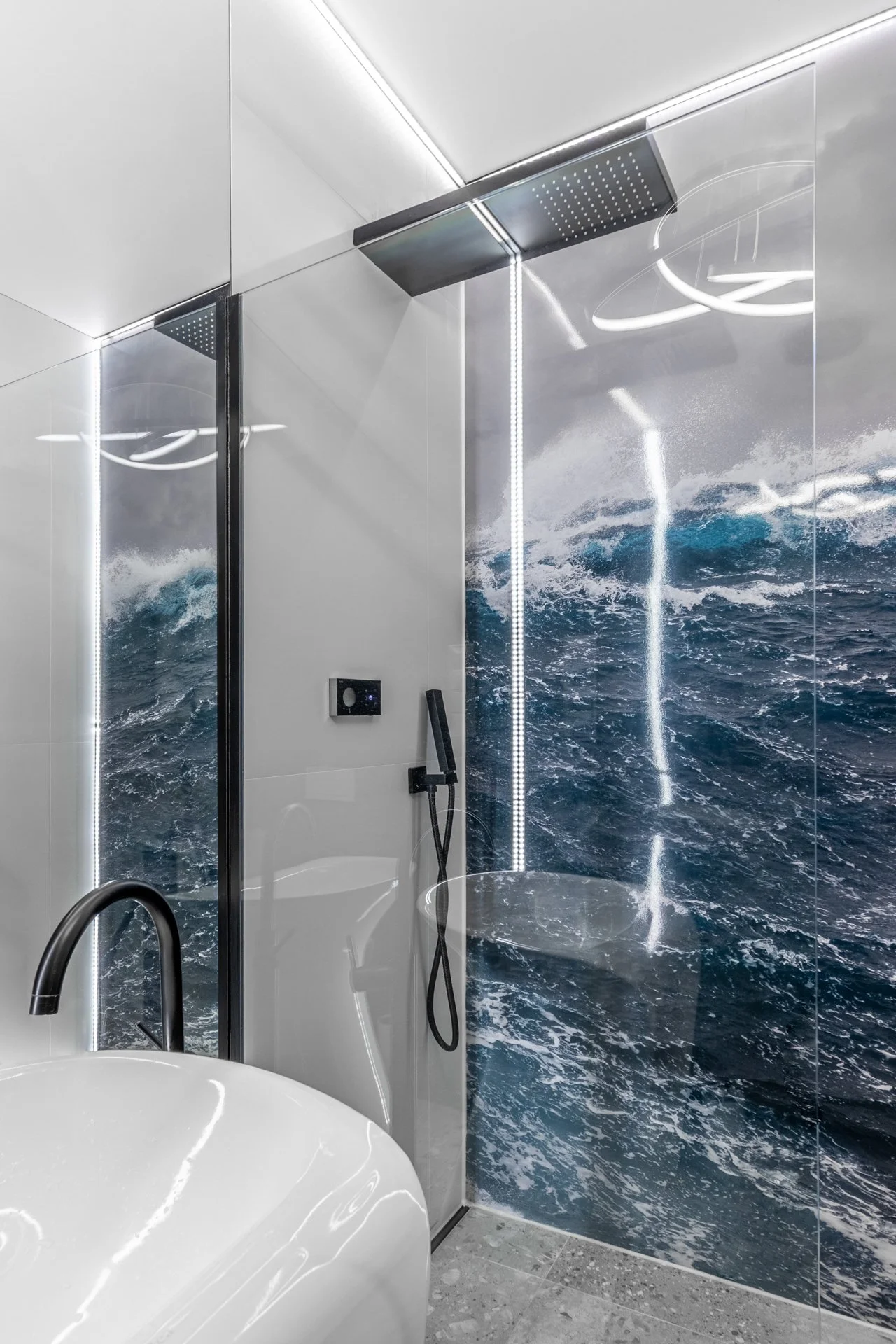 Modern bathroom with a large wall mural of the ocean waves, a shower area with black fixtures, and a white bathtub.