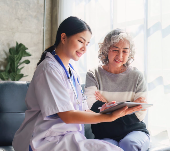 A nurse showing a tablet to an elderly woman in a bright room.