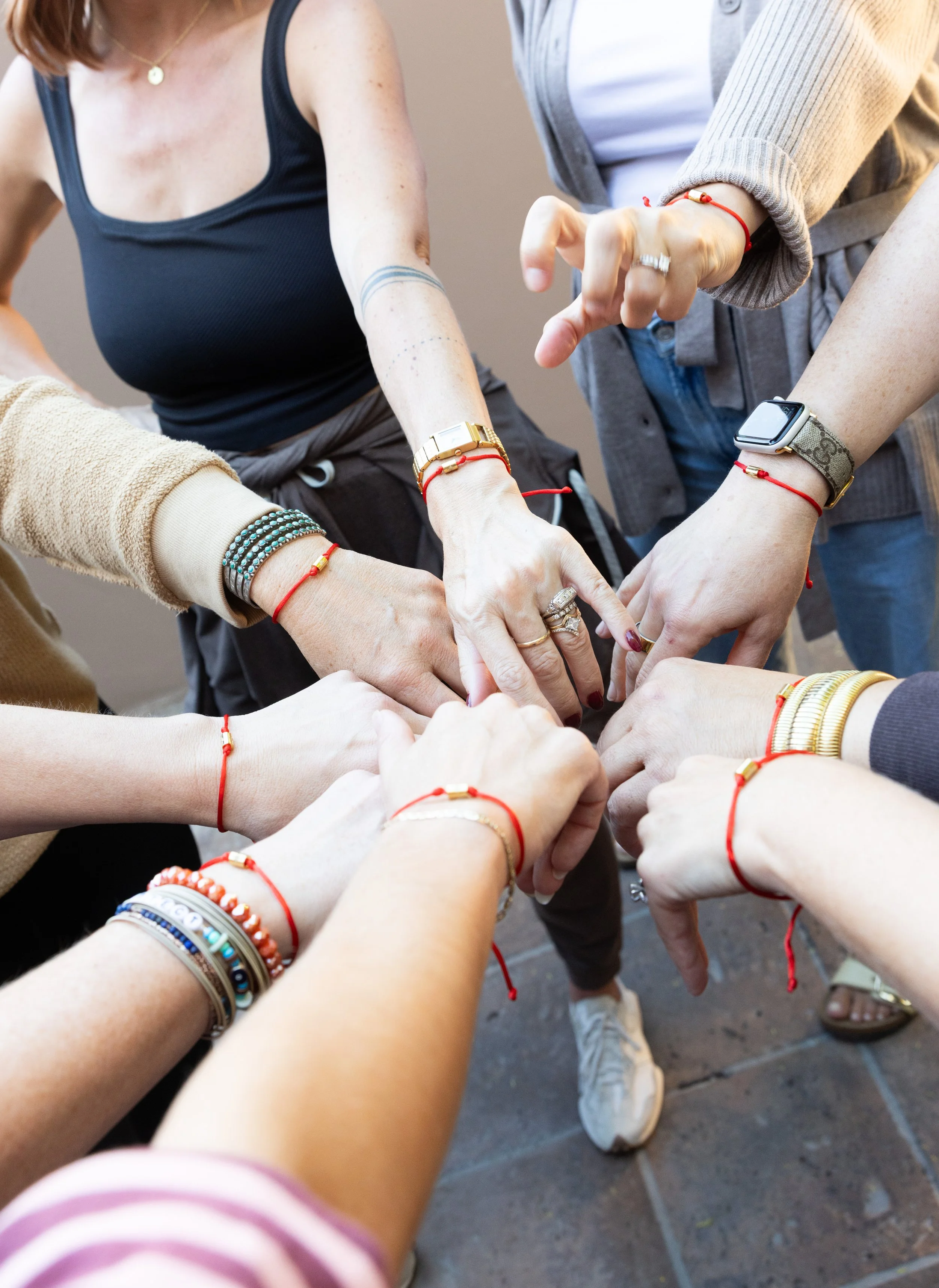 A group of people learning about retreat operations support stand in a circle, each wearing a red string bracelet on their wrist.