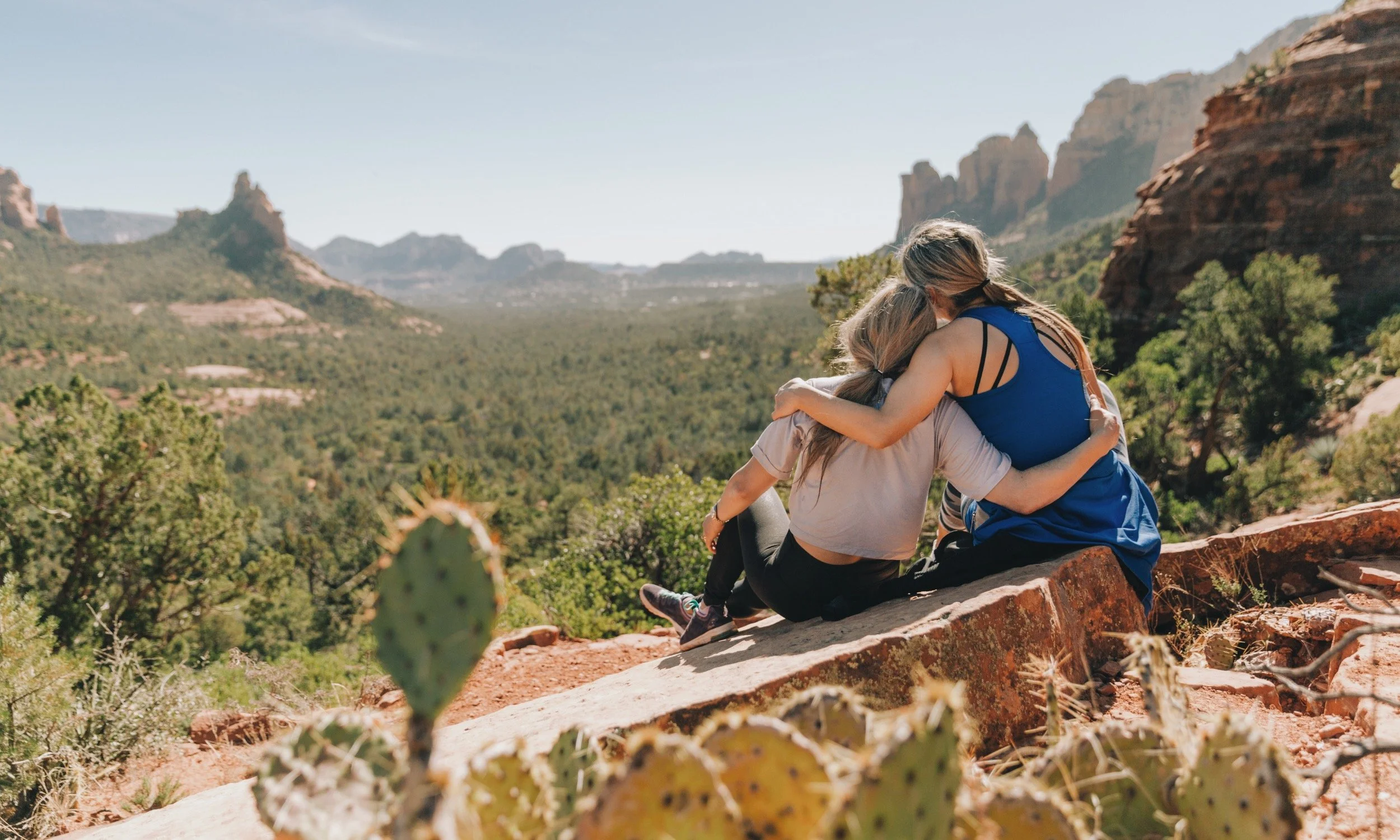 Two women sitting on a rock side hugging through learning done for you retreat planning.