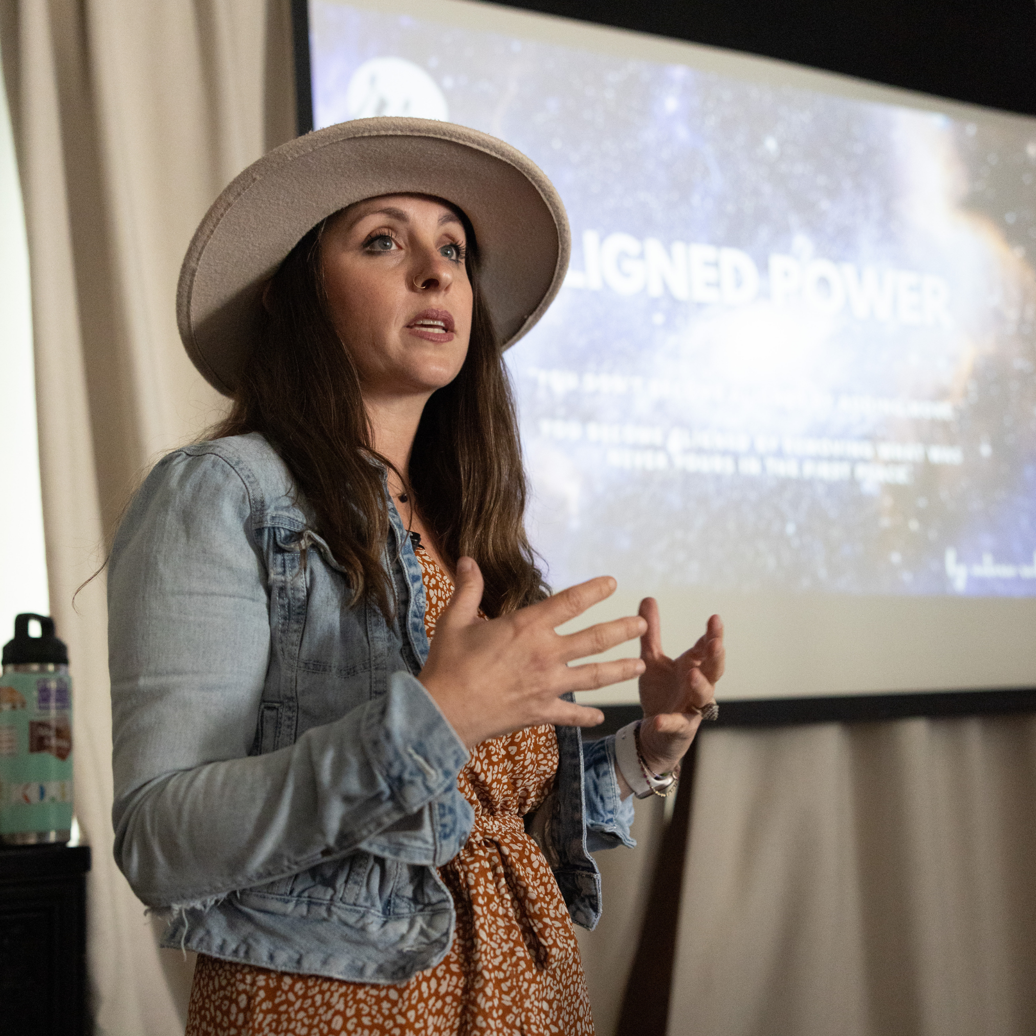 Woman wearing a hat speaks in front of a projected presentation about retreat planning tools in a room.