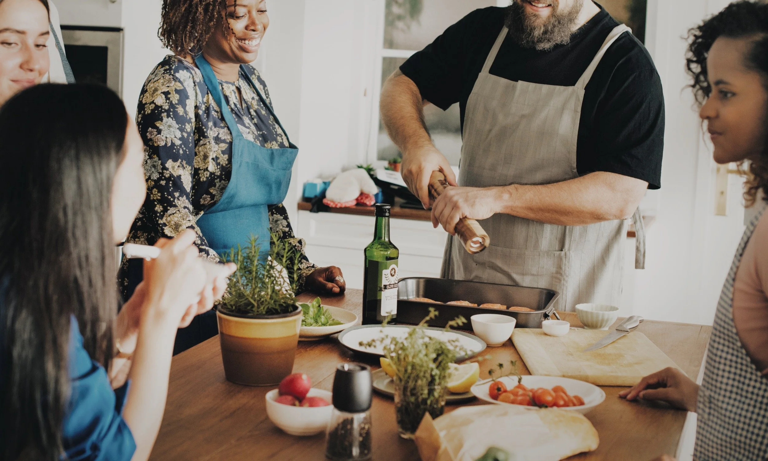 Four people prepare food together in a kitchen, smiling and talking around a table with fresh ingredients to represent done with you retreat planning.