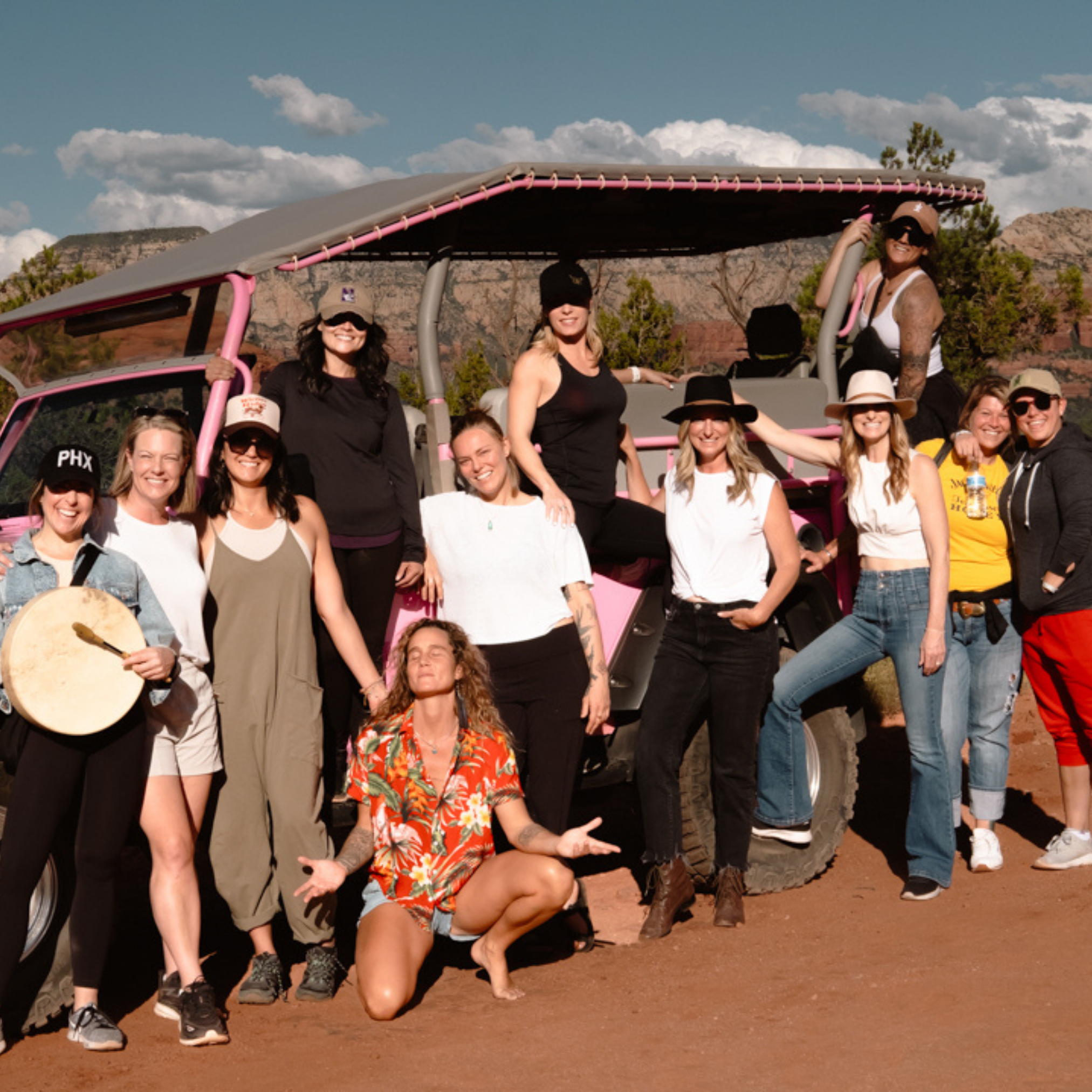 A group of people pose together outdoors in front of a pink off-road vehicle on a sunny day for retreat marketing support.