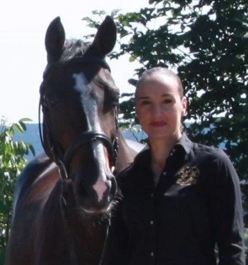 Frau mit Glatze und schwarzes Hemd neben einem schwarzen Pferd im Freien bei Sonne