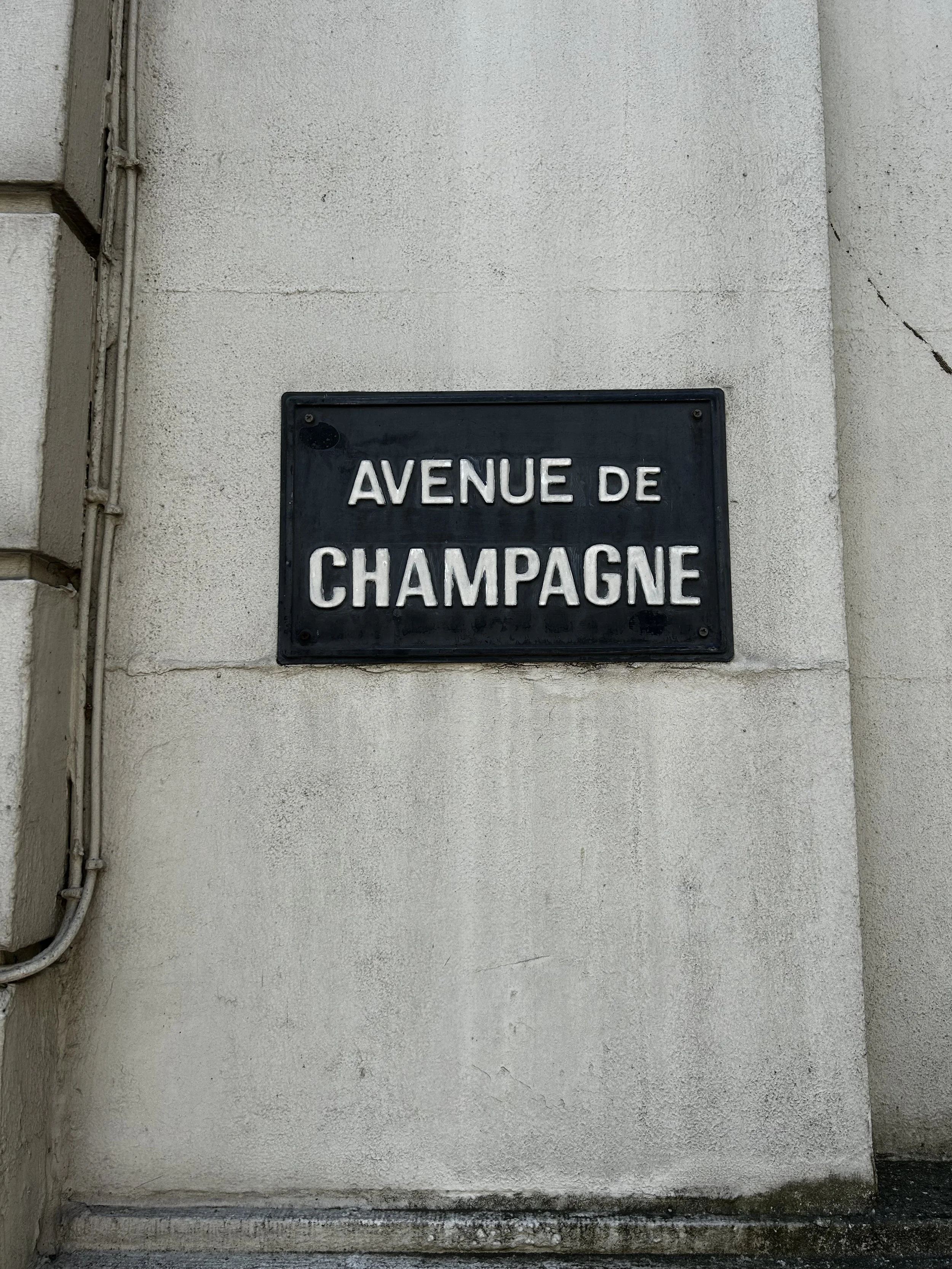Street sign on a wall reading 'Avenue de Champagne' in French.