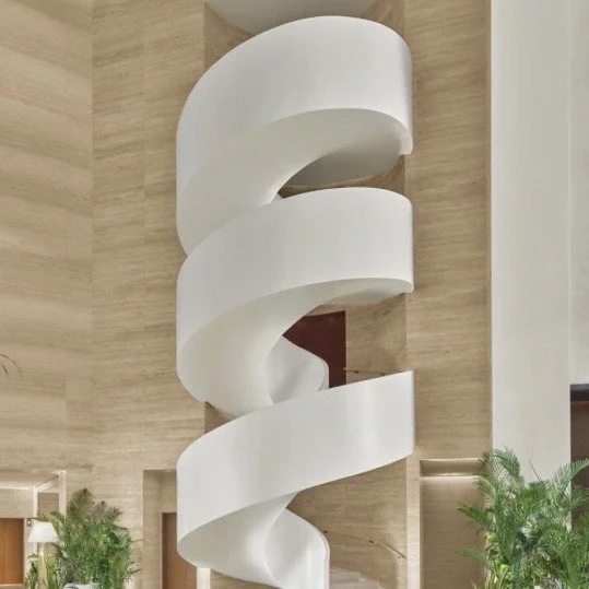 Modern white spiral staircase in a spacious indoor setting with wooden accents and green plants.