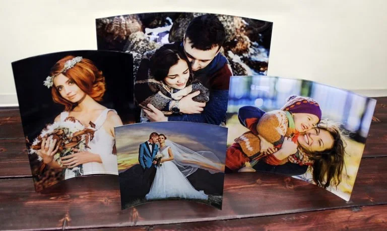 Collection of five large printed photographs of couples and a woman, displayed on a wooden surface. The images include a woman with red hair holding a bouquet, a couple hugging outdoors, a wedding couple, and two children playing.