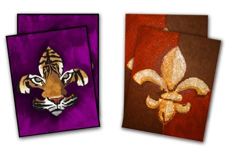 Two sets of artistic cards, one with a tiger face on a purple background and the other with a fleur-de-lis symbol on a red background.