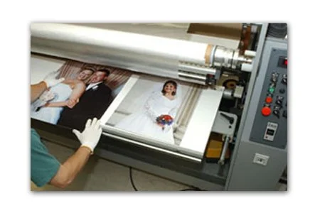 A person working on a large format printing machine printing a portrait of a woman holding a bouquet of flowers.