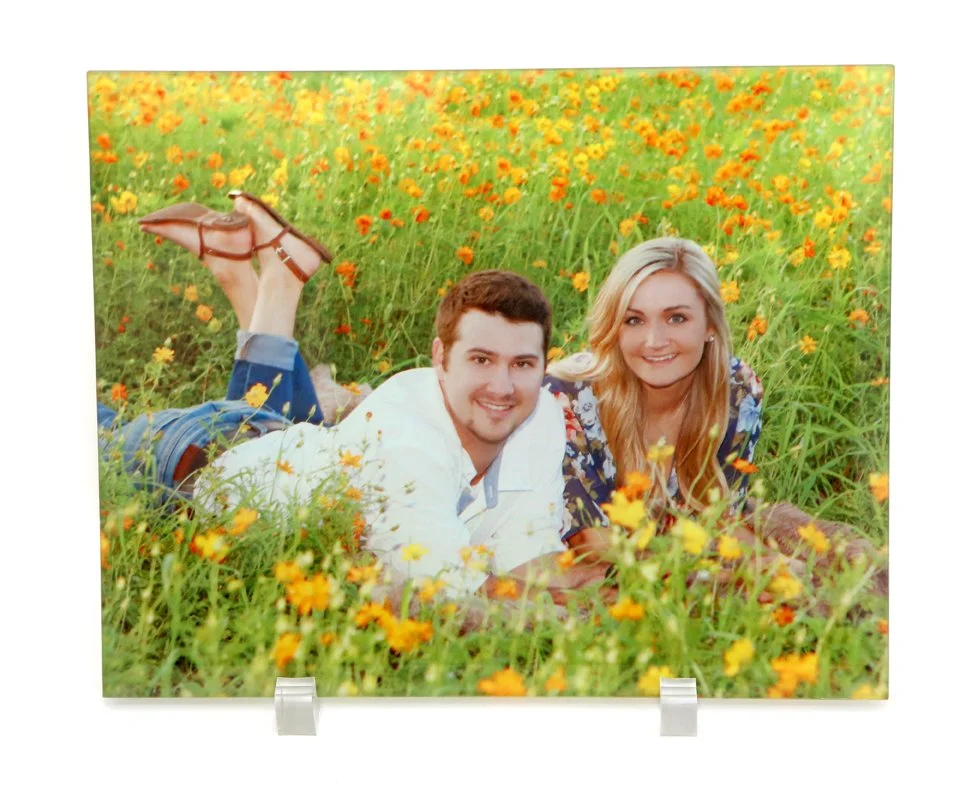 A young man and woman lying in a field of yellow and orange flowers, smiling at the camera.
