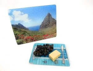 A postcard with a mountain landscape, a plate with black grapes, a stick of butter, and a butter knife placed on a blue striped cloth.