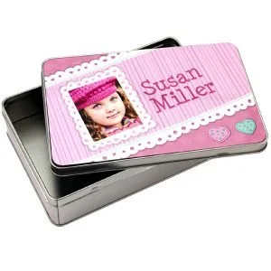 A tin box with a pink striped lid featuring a photo of a young girl in a pink hat, the name 'Susan Miller' in pink text, and decorated with small heart illustrations.