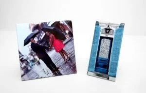 Photo of a small photo stand with a picture of two people walking in the rain, holding umbrellas. Next to it is a blue and silver cardholder or paper holder.