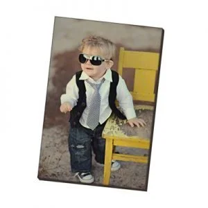 Young child wearing sunglasses, a white shirt, black vest, and tie, standing next to a yellow chair.