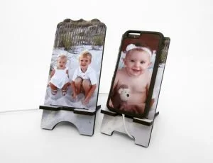 Two picture frames on stands, one with a photo of three children sitting outdoors and the other with a close-up photo of a smiling baby on a smartphone.