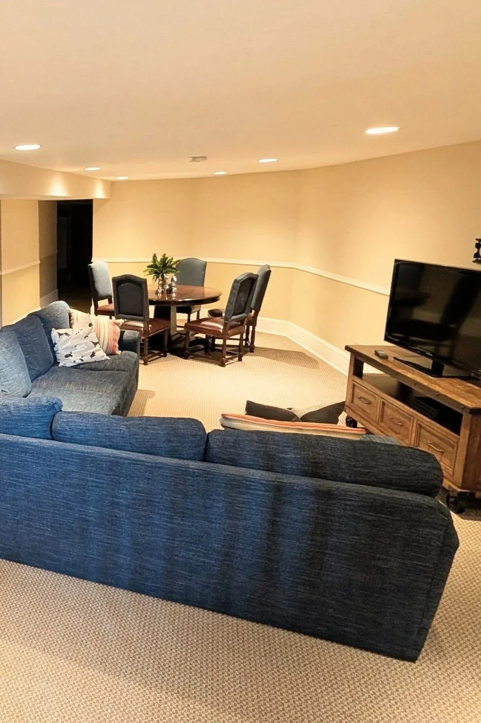 A view into the family room in the basement of the Moore House, with a large sectional, TV, and game table.