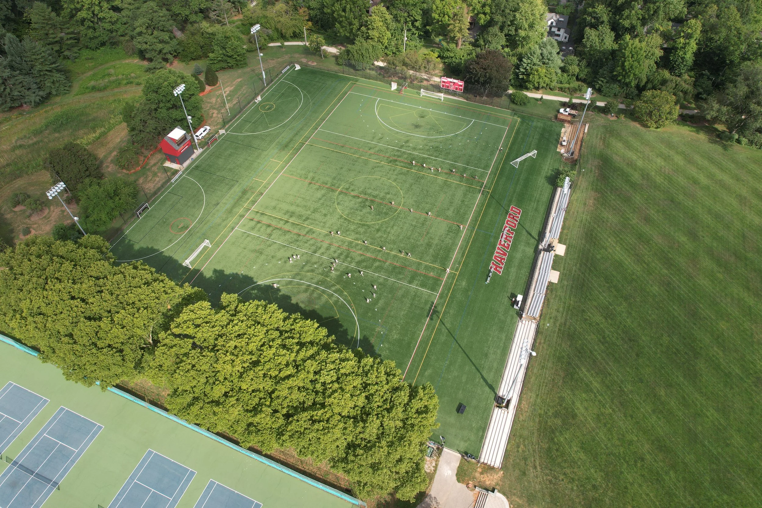 Aerial view of a sports complex featuring tennis courts, a multi-purpose field, and soccer fields surrounded by trees.