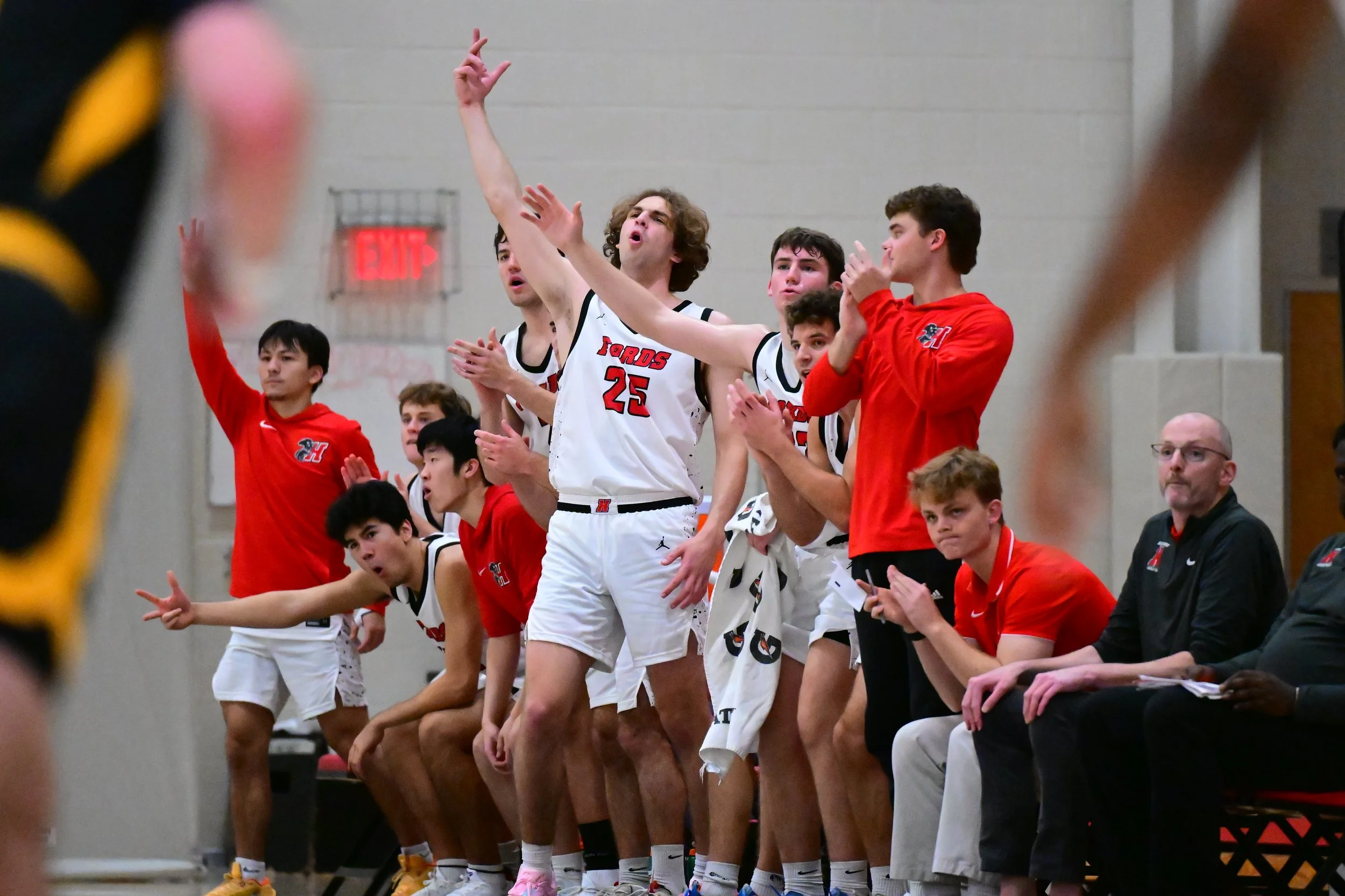 A group of Haverford Men's Basketball players and the coaching staff standing near the bench, with some clapping and others celebrating, during a game at Gooding Arena.