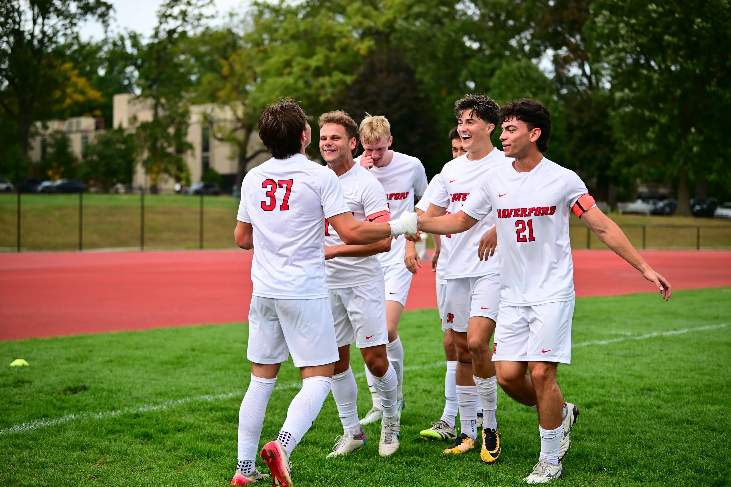 Haverford men's soccer players in white uniforms celebrate together on the field after a goal.
