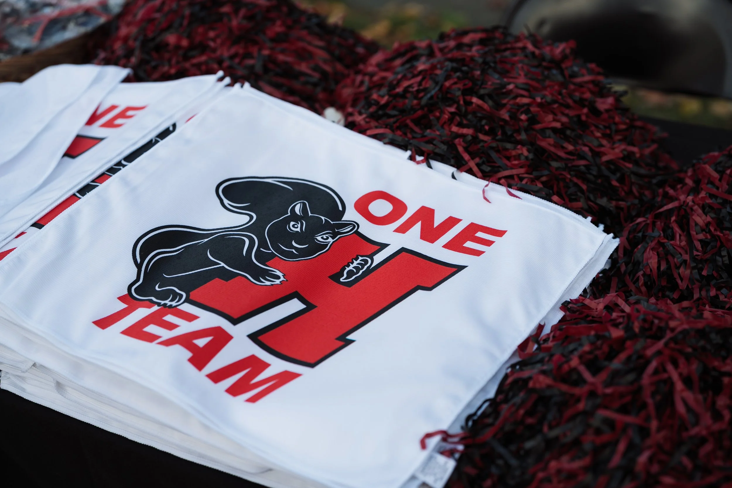 A white fabric item with a black and white panther logo and red text, laid on a red and black shredded material.
