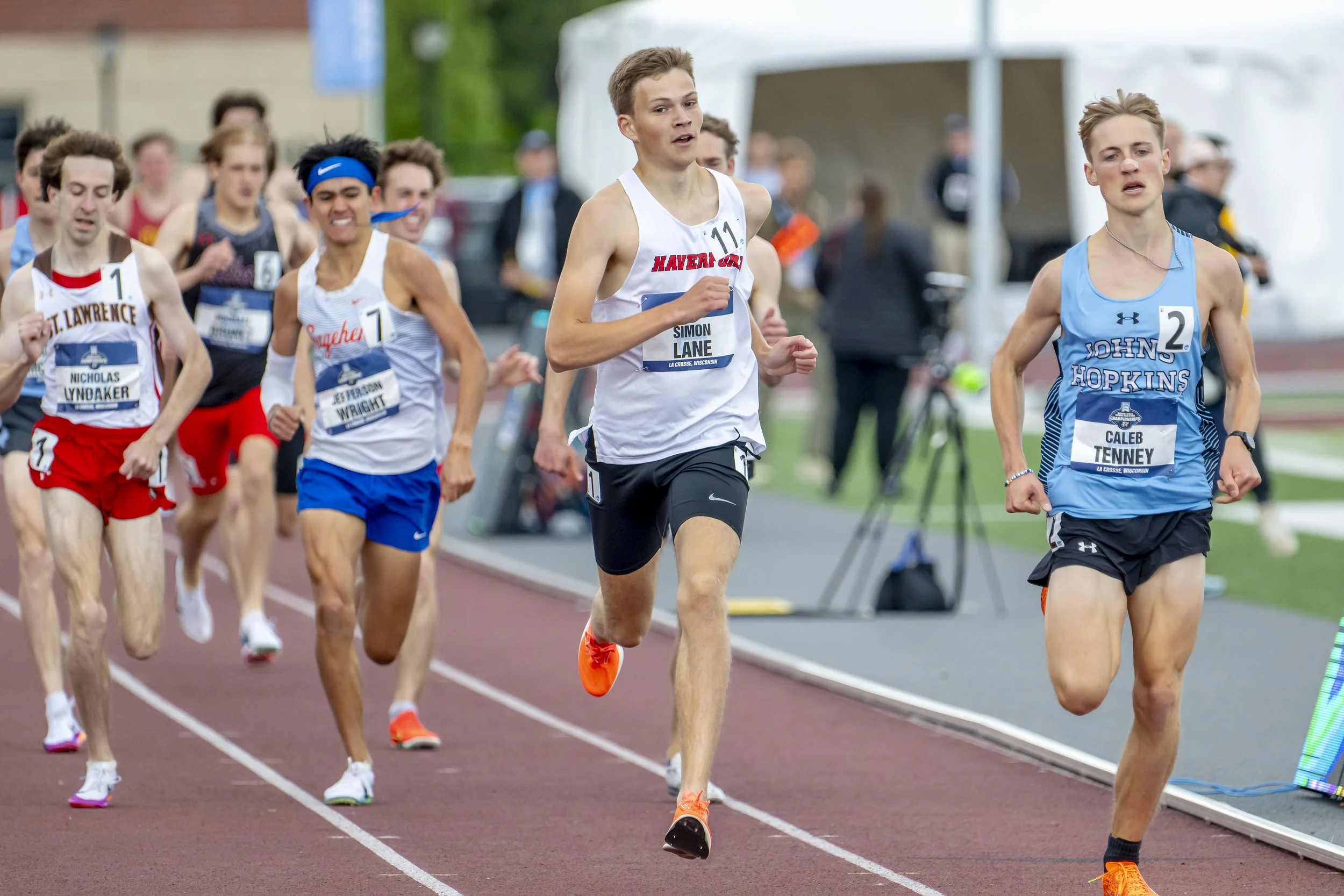 A group of young male runners participating in a track race outdoors.