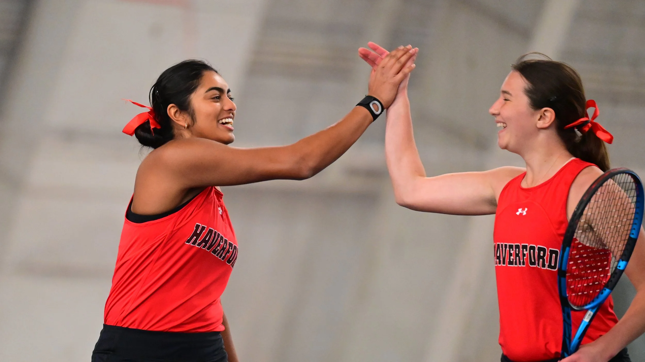 Two female tennis players high fiving on an indoor tennis court.