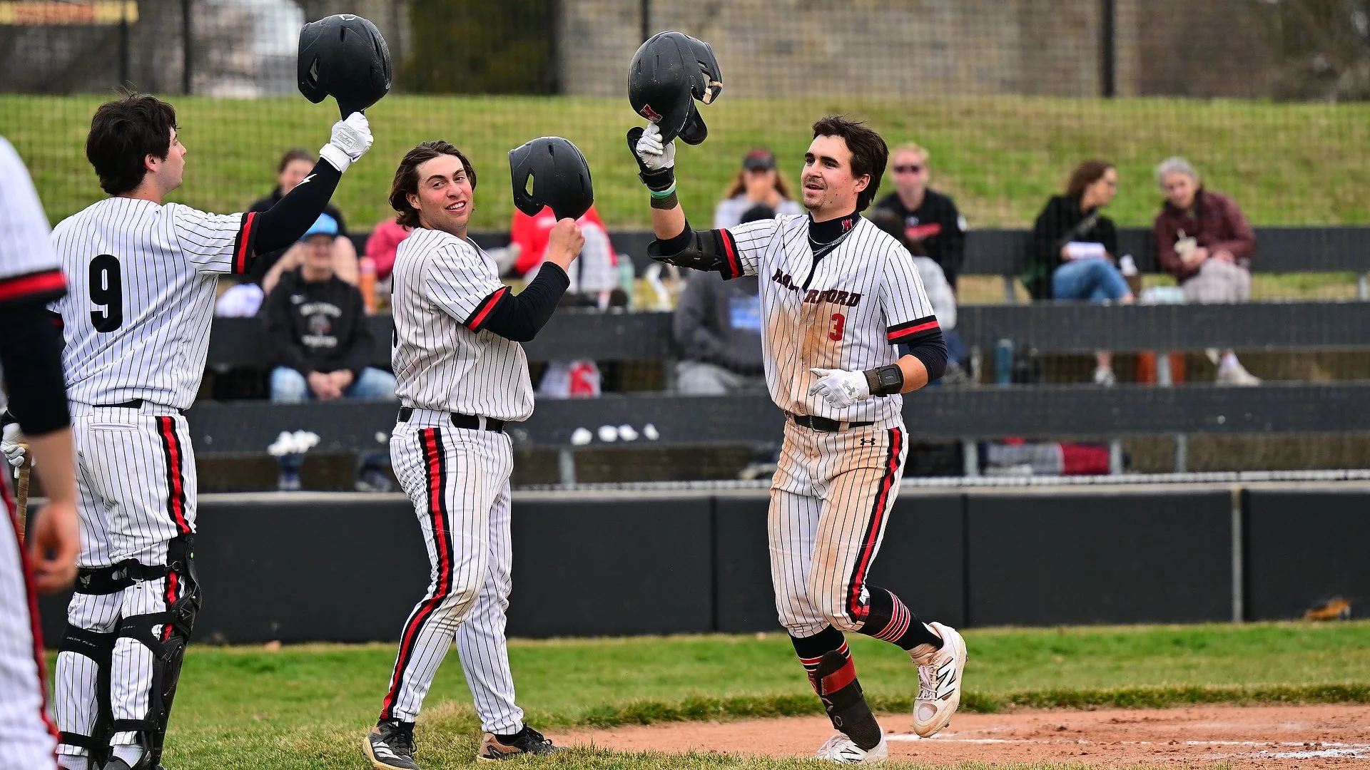 A group of Haverford baseball players raising their helmets with fans in the background.