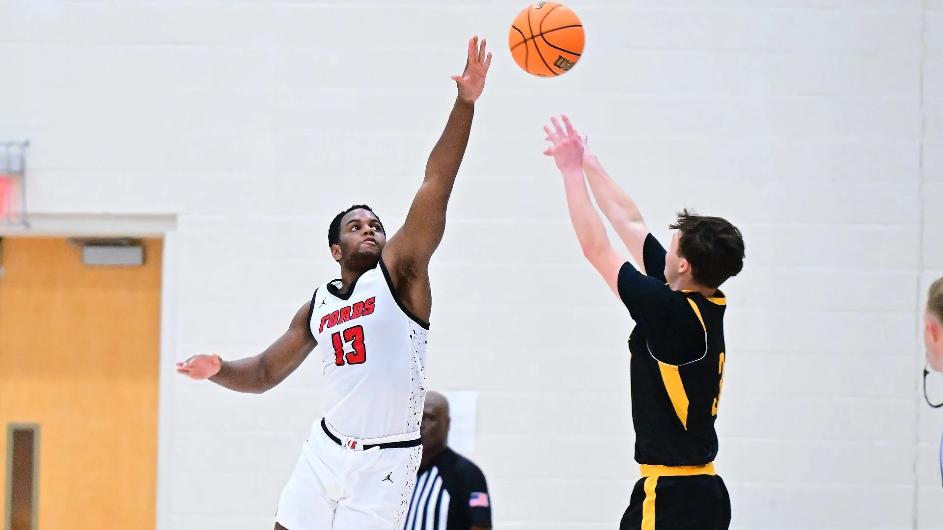A Haverford men's basketball player contests a jump shot during a game as both players reach for the ball.
