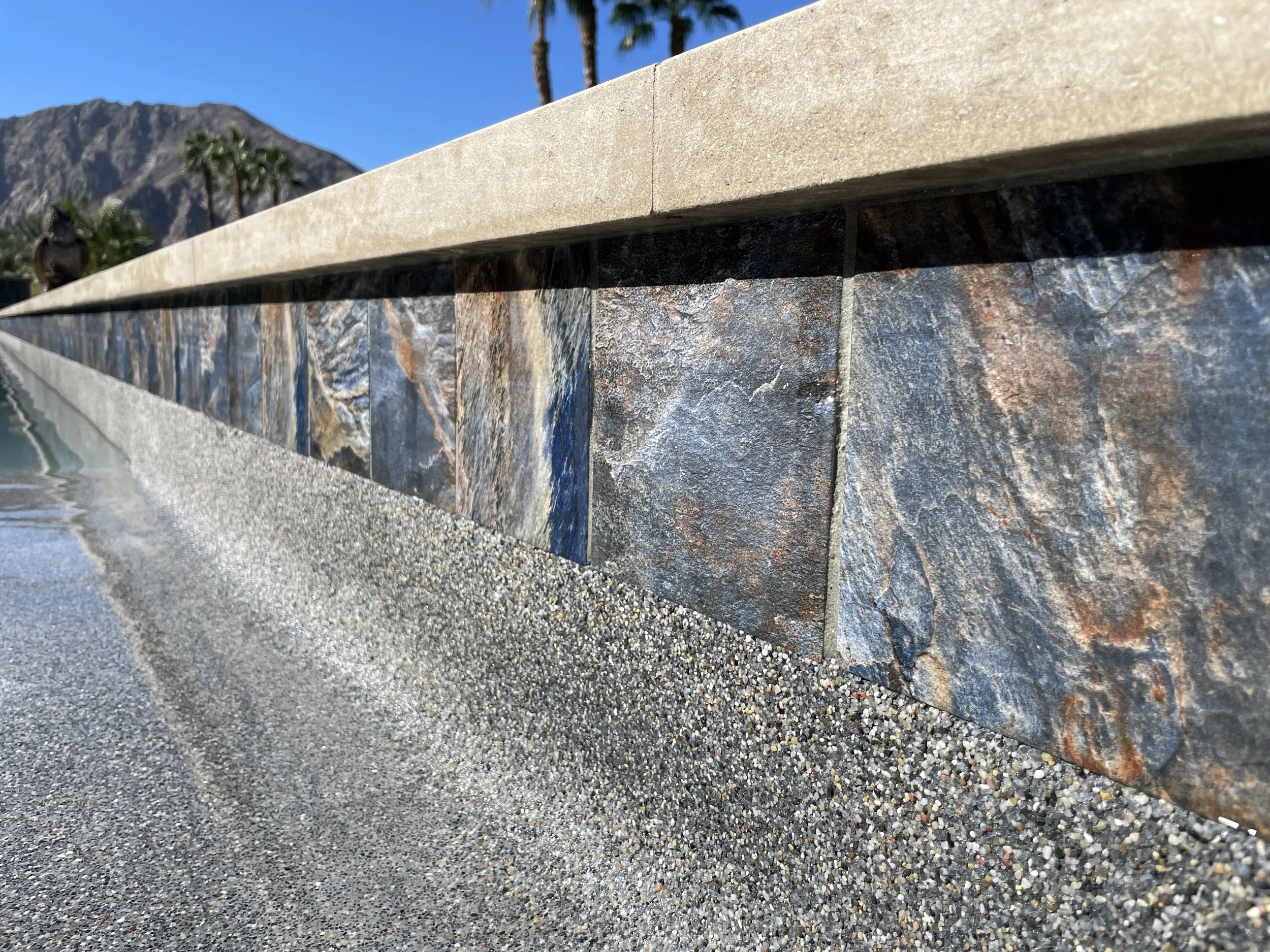 Close-up of a stone and concrete wall with a mountain and palm trees in the background, clear blue sky